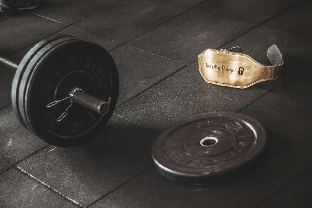 a barbell, a plate and a support belt lying on the ground in a gym